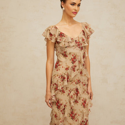 Woman wearing a long flared maxi dress with ruffles and floral print pattern in pastel colors standing outdoors