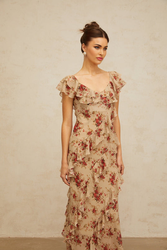 Woman wearing a long flared maxi dress with ruffles and floral print pattern in pastel colors standing outdoors