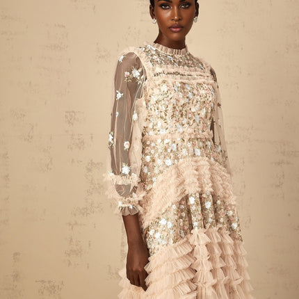 Woman wearing a long floral embroidered tulle maxi dress with tiered skirt in soft pastel colors against a plain background