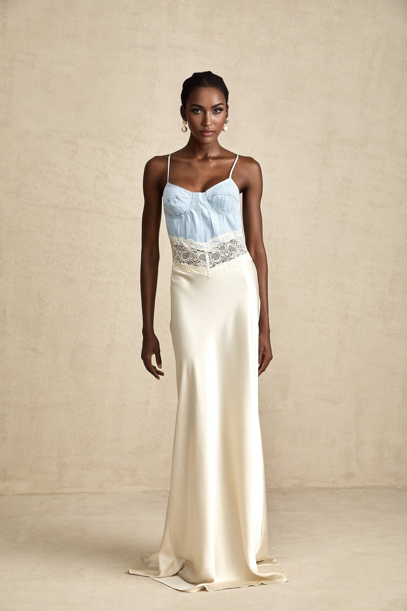 Woman wearing a long flowing maxi dress with lace trim and paneled design in a light color standing against a plain background