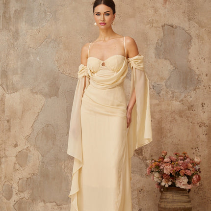 Woman wearing a long flowy neutral colored chiffon maxi dress with ruched details