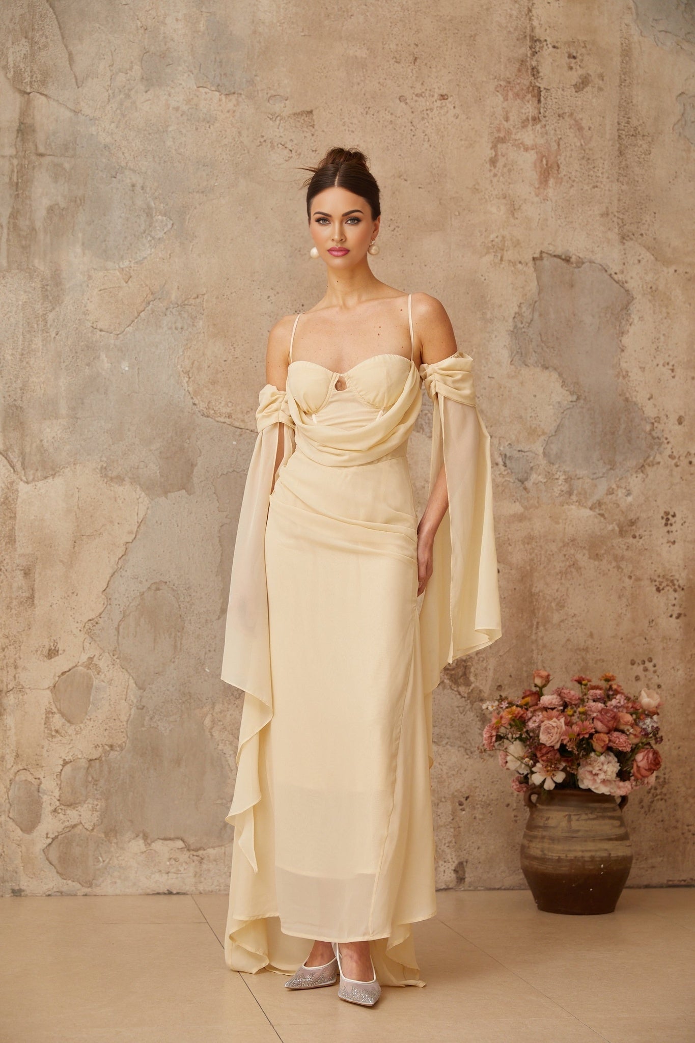 Woman wearing a long flowy neutral colored chiffon maxi dress with ruched details