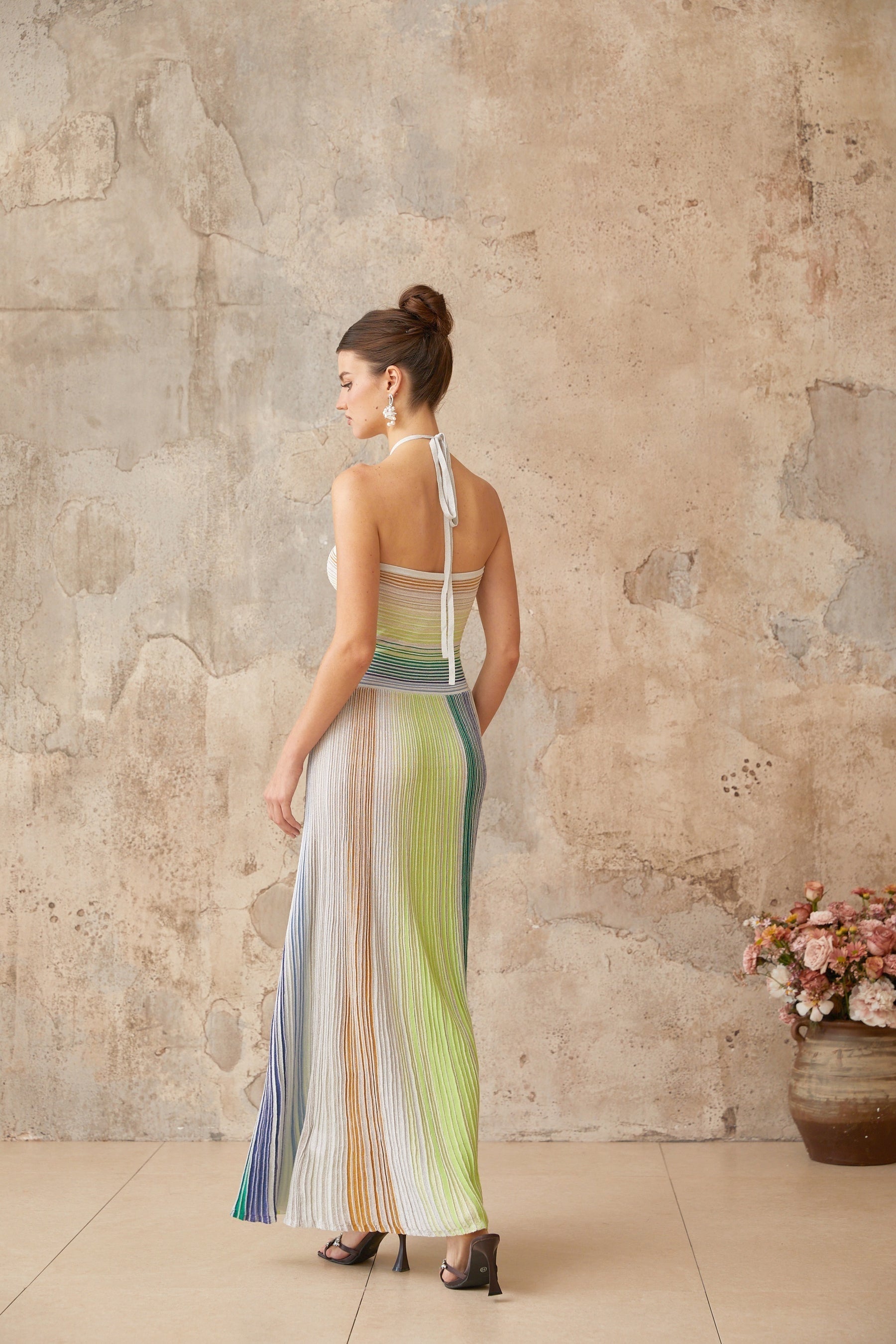 Woman wearing a long metallic knit maxi dress with backless design standing in elegant pose
