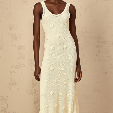 Woman wearing a long white maxi dress with floral embroidery and crochet knit details standing in a garden setting