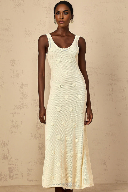 Woman wearing a long white maxi dress with floral embroidery and crochet knit details standing in a garden setting