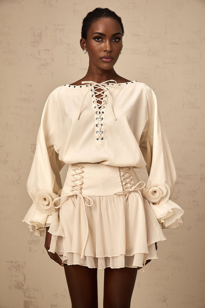 Woman wearing a matching blouse and skirt set in light fabric The blouse has ruffles and a self tie detail The skirt is flowy and coordinated with the top