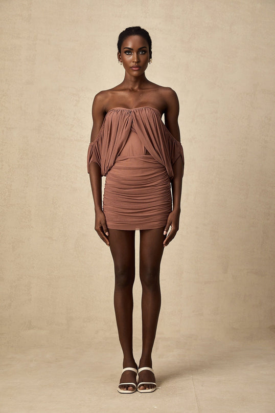 Woman wearing a matching offshoulder bodysuit and skirt set in a light color standing against a plain background