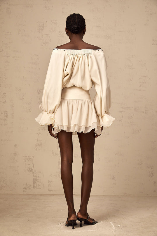 Woman wearing a matching ruffled blouse and skirt set in light fabric with self tie details and feminine silhouette