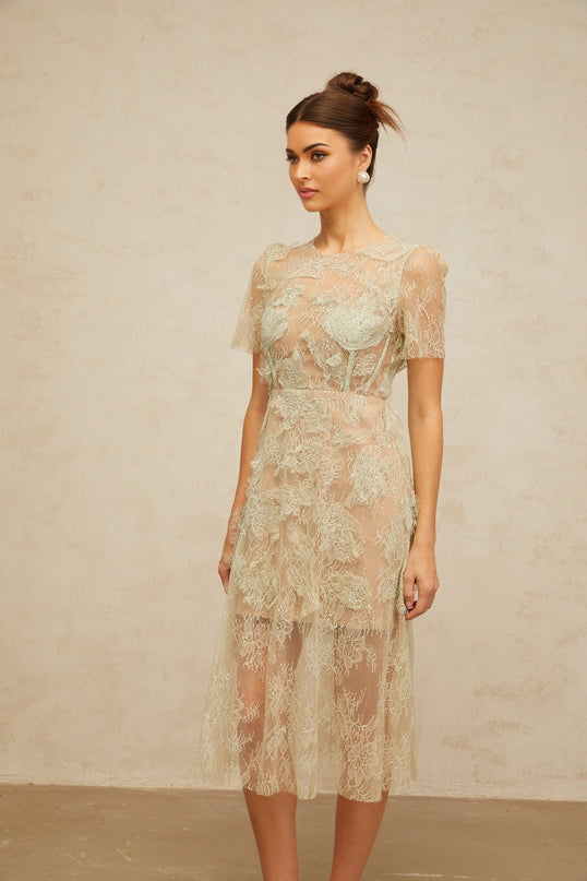 Woman wearing a mintgreen midi dress with floral lace pattern standing in a neutral background