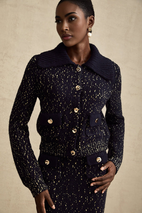 Woman wearing a navy blue crochet knit jacket and matching skirt set standing against a plain background