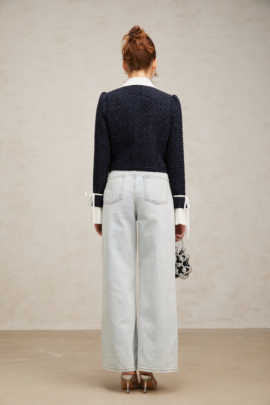 Woman wearing a navy blue tweed jacket with panels standing against a plain background