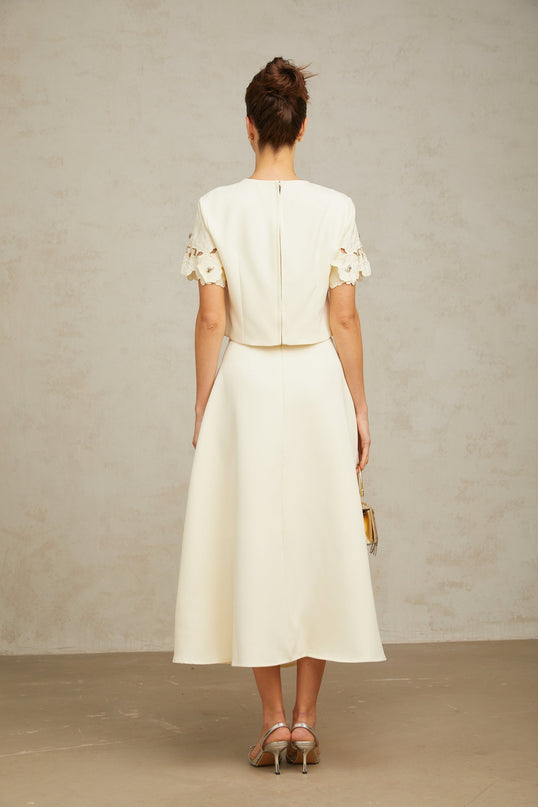 Woman wearing a neutral colored matching set consisting of a top and skirt with 3D petal details