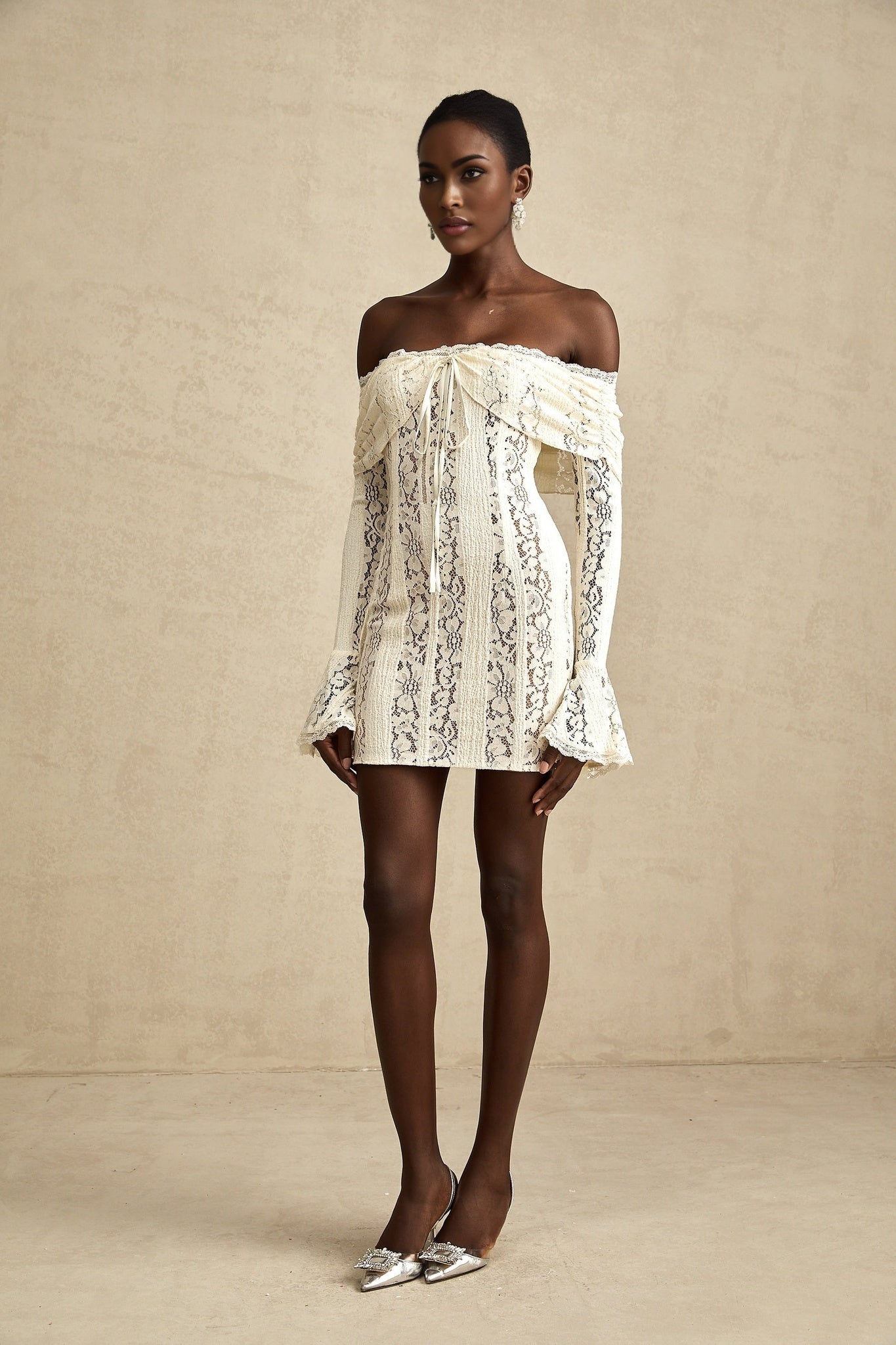 Woman wearing a neutral colored mini dress with floral lace pattern and flared cuffs