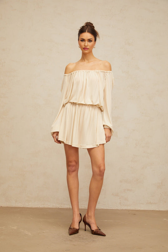 Woman wearing a neutral colored mini dress with structured design details standing in front of plain background