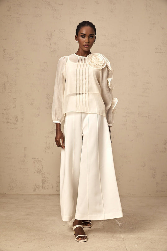 Woman wearing a neutral colored semi sheer blouse with 3d flower details on the fabric