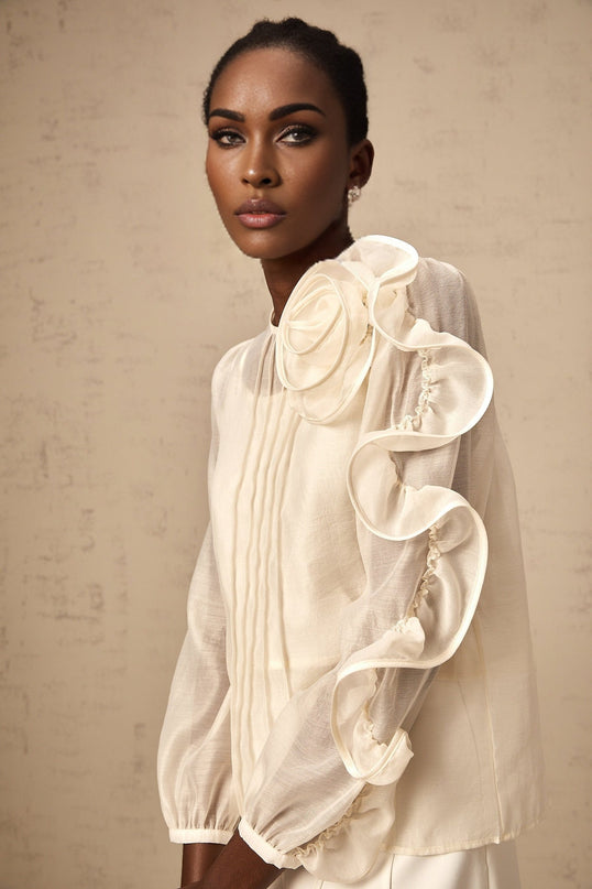 Woman wearing a neutral colored semi sheer blouse with 3d flower details