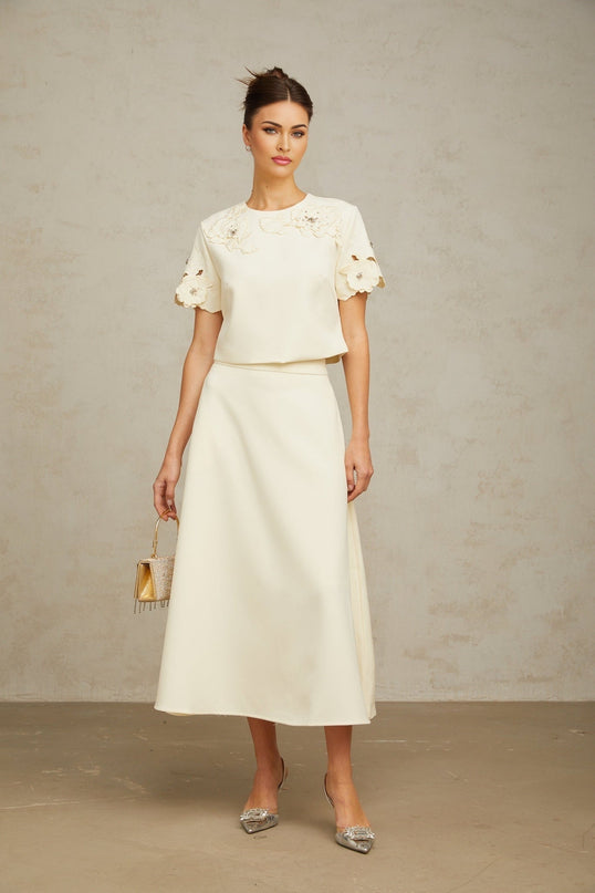 Woman wearing a neutralcolored matching set consisting of a top and skirt with 3D petal details