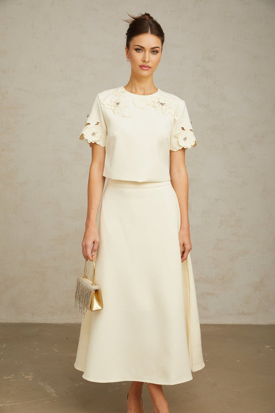 Woman wearing a neutralcolored matching set with a top and skirt featuring threedimensional petal details