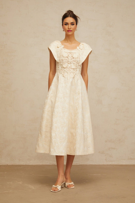 Woman wearing a neutralcolored midi dress with floral embroidery and embellishments standing in a relaxed pose