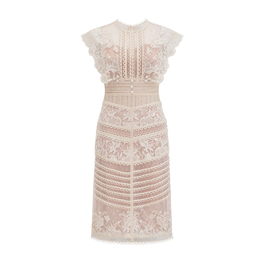 Woman wearing a neutralcolored midi dress with floral embroidery and lace details standing in a relaxed pose