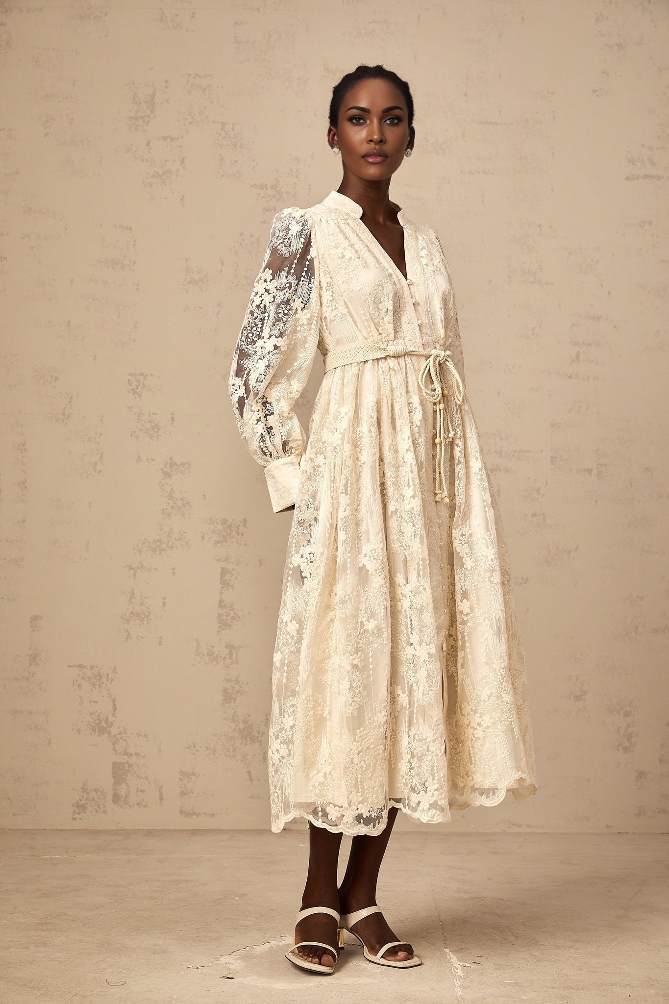 Woman wearing a neutralcolored midi dress with lace embroidery details standing in a casual pose