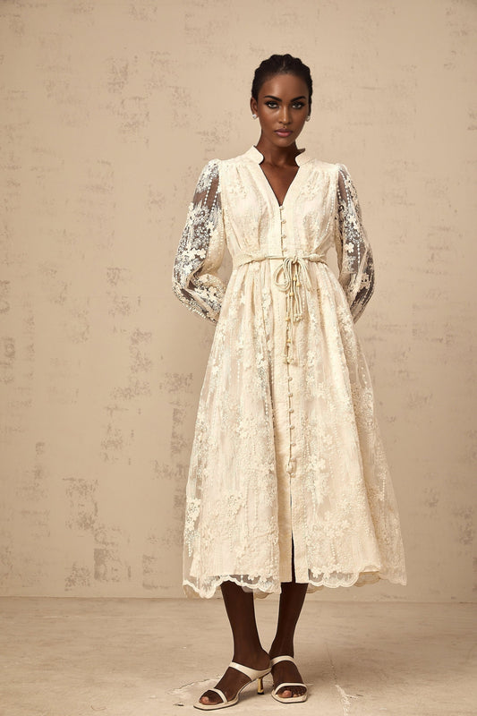 Woman wearing a neutralcolored midi dress with lace embroidery details standing in a casual pose