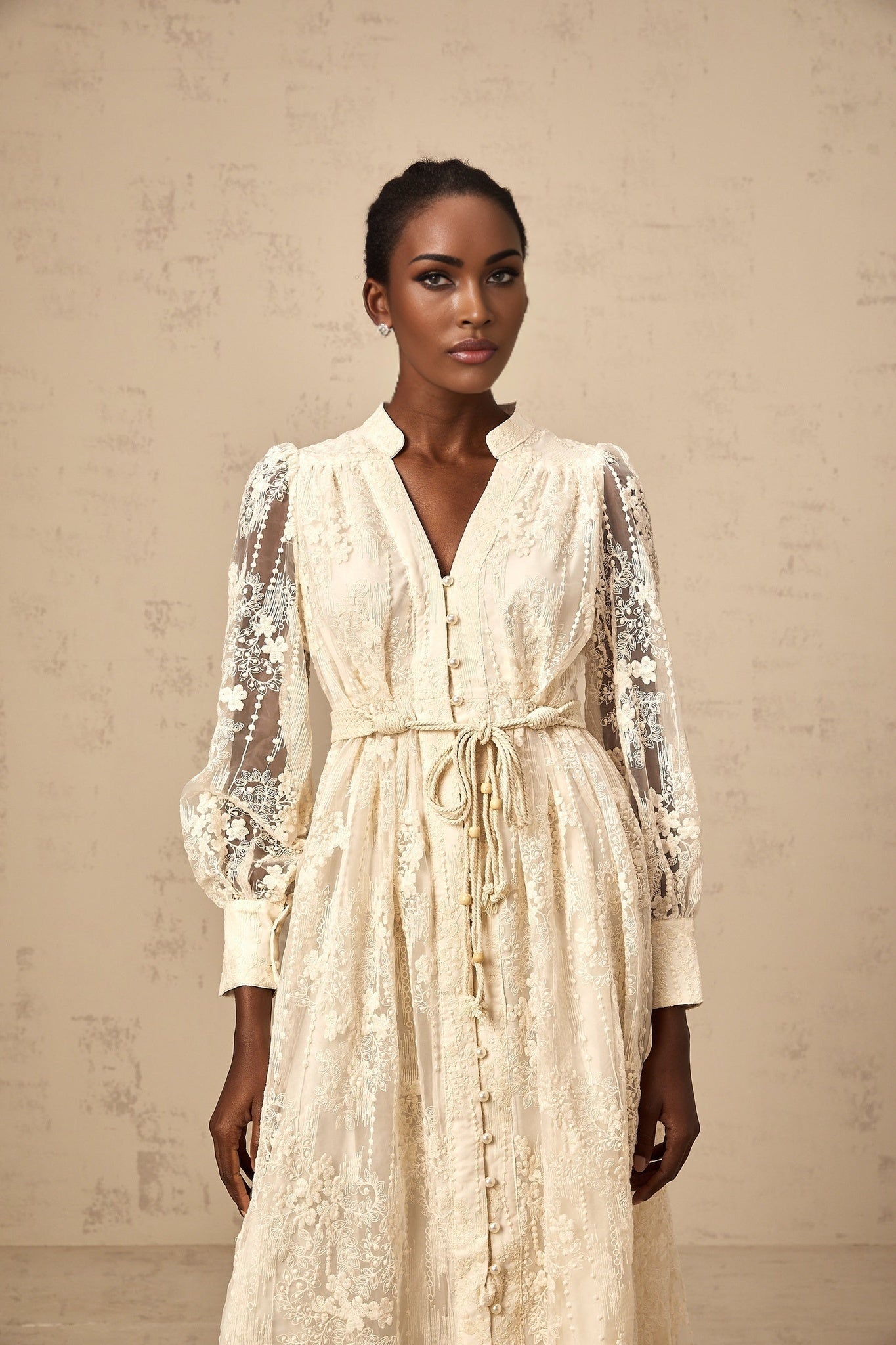 Woman wearing a neutralcolored midi dress with lace embroidery details standing in a relaxed pose