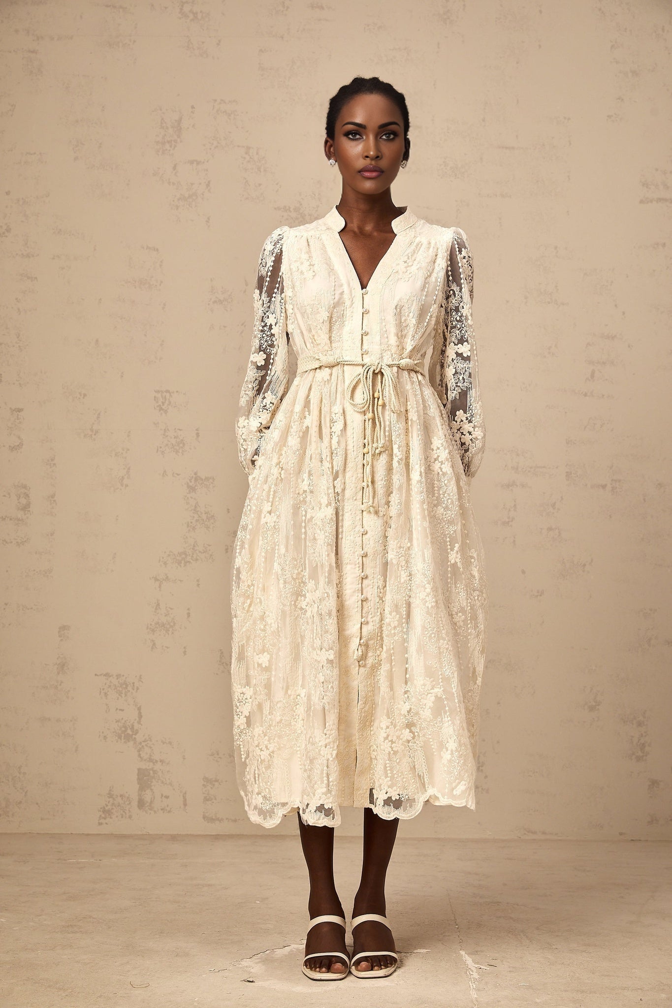 Woman wearing a neutralcolored midi dress with lace embroidery details standing in a relaxed pose