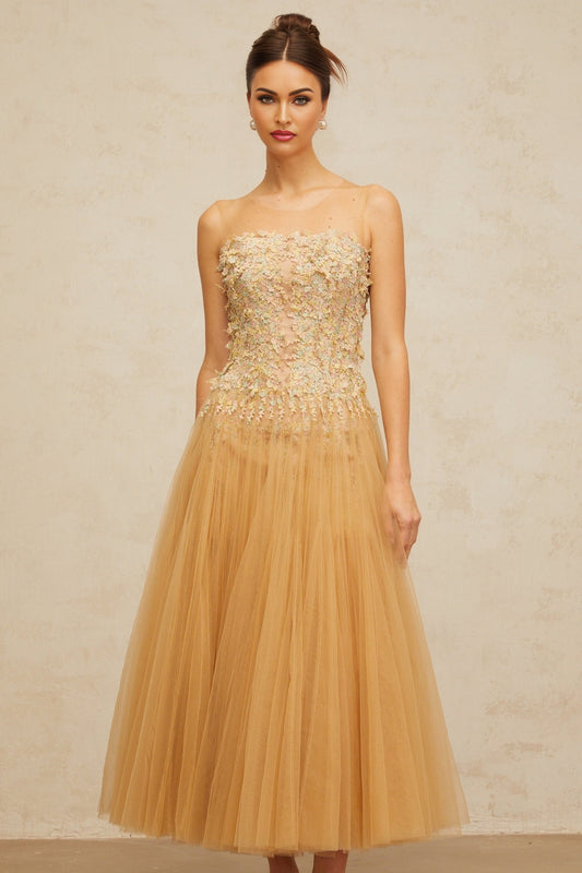 Woman wearing a neutralcolored midi dress with pleated tulle and sequin details standing in a soft pose