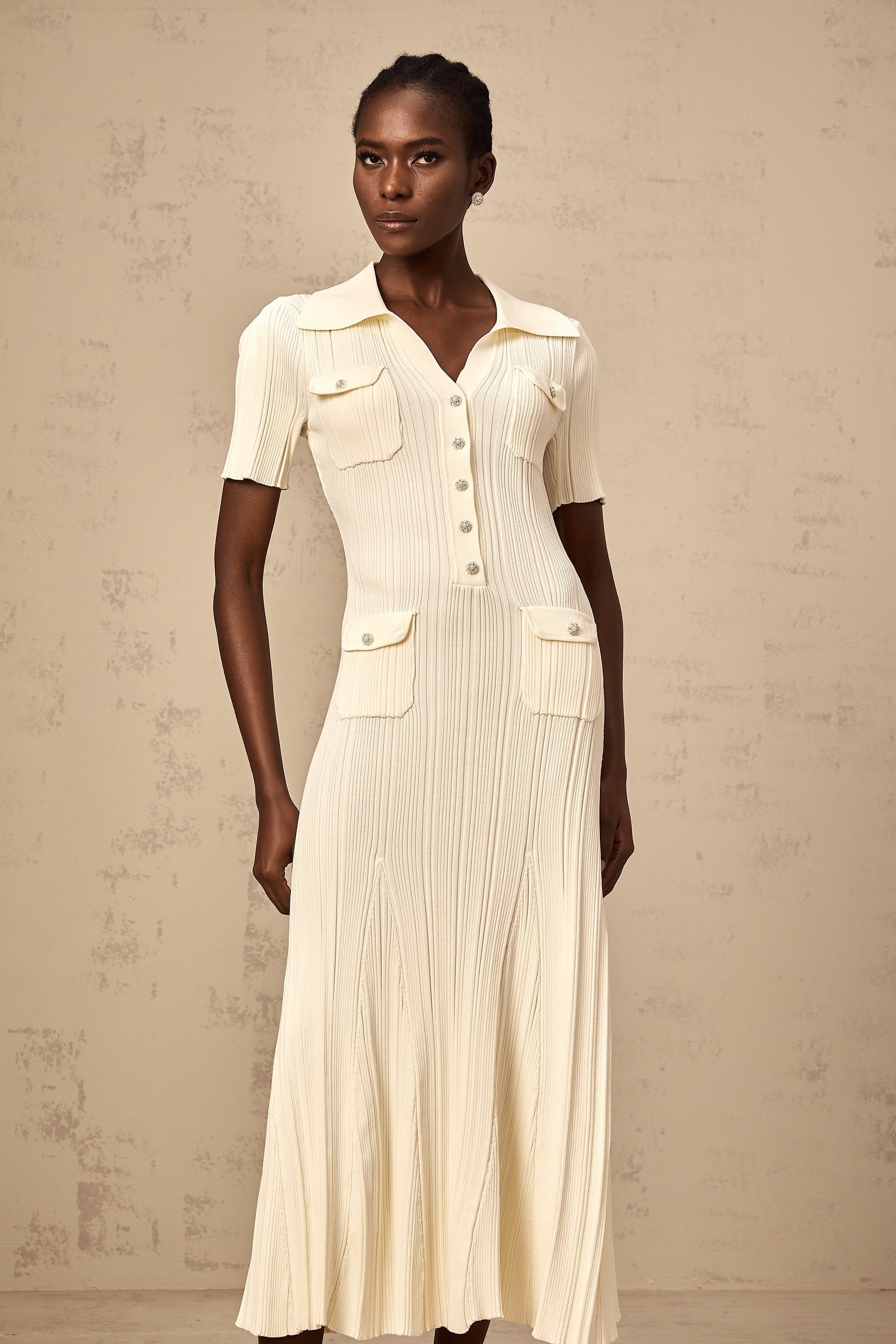 Woman wearing a neutralcolored ribbedknit midi dress with long sleeves standing against a plain background