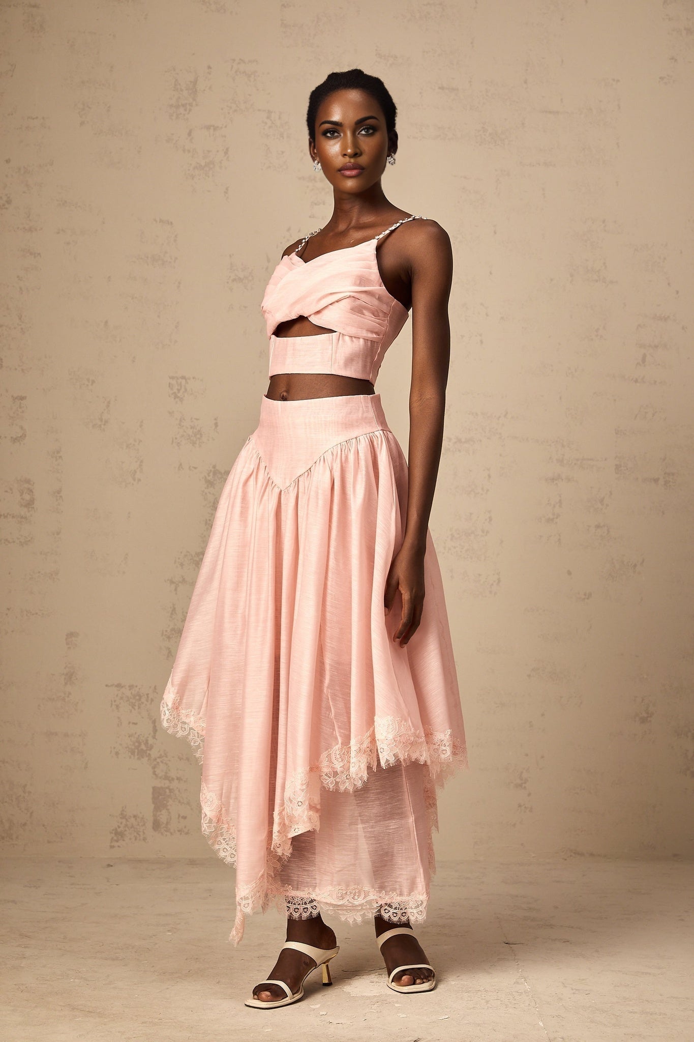 Woman wearing a pink matching set with an asymmetric ruffled top and skirt The top features a one shoulder design with ruffles while the skirt has a coordinating ruffle detail