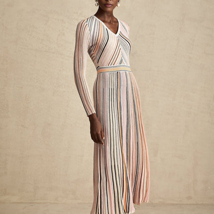 Woman wearing a pink metallic pleated midi dress with a flowing skirt and fitted bodice standing against a plain background