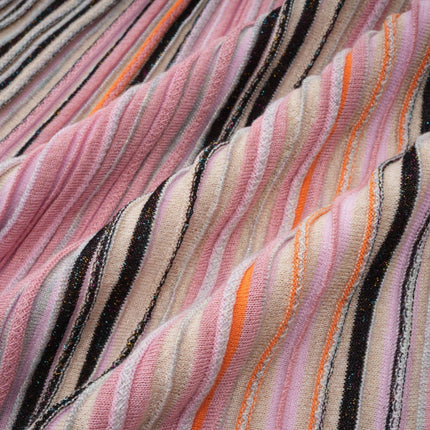 Woman wearing a pink metallic pleated midi dress with a flowing skirt and fitted bodice standing in a neutral background