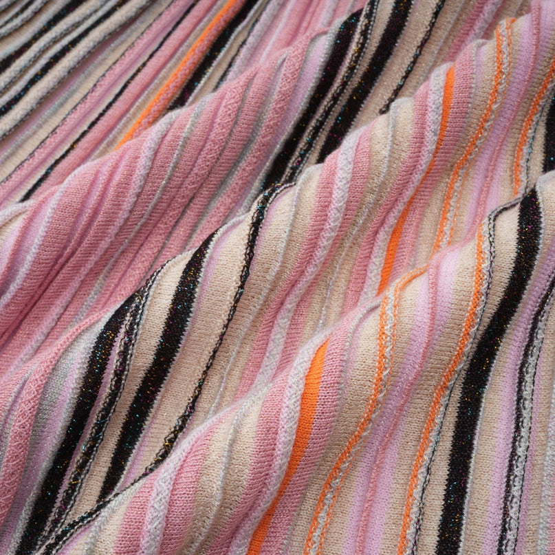 Woman wearing a pink metallic pleated midi dress with a flowing skirt and fitted bodice standing in a neutral background