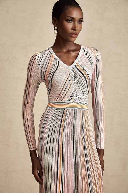 Woman wearing a pink metallic pleated midi dress with a flowy skirt and fitted bodice standing in a neutral background