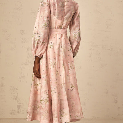 Woman wearing a pink midi dress with floral print and embellishments standing against a plain background