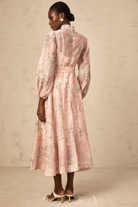 Woman wearing a pink midi dress with floral print and embellishments standing against a plain background