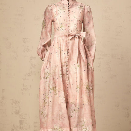 Woman wearing a pink midi dress with floral print and embellishments standing in a neutral background