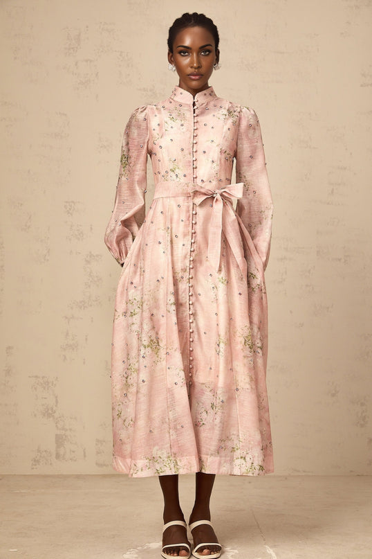 Woman wearing a pink midi dress with floral print and embellishments standing in a neutral background