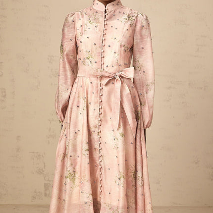 Woman wearing a pink midi dress with floral print and embellishments standing in a neutral background