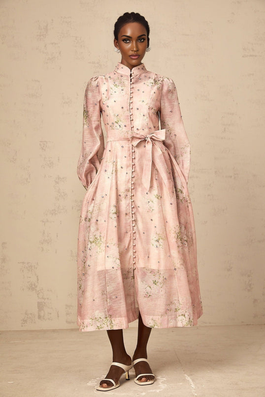 Woman wearing a pink midi dress with floral print and embellishments standing in a neutral background