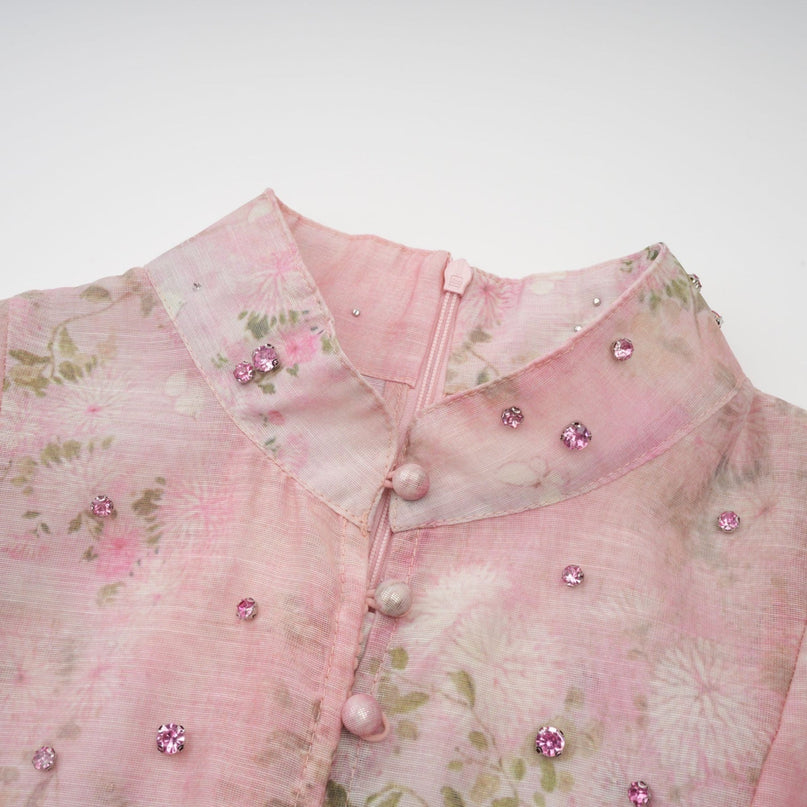 Woman wearing a pink midi dress with floral print and embellishments standing in a neutral background