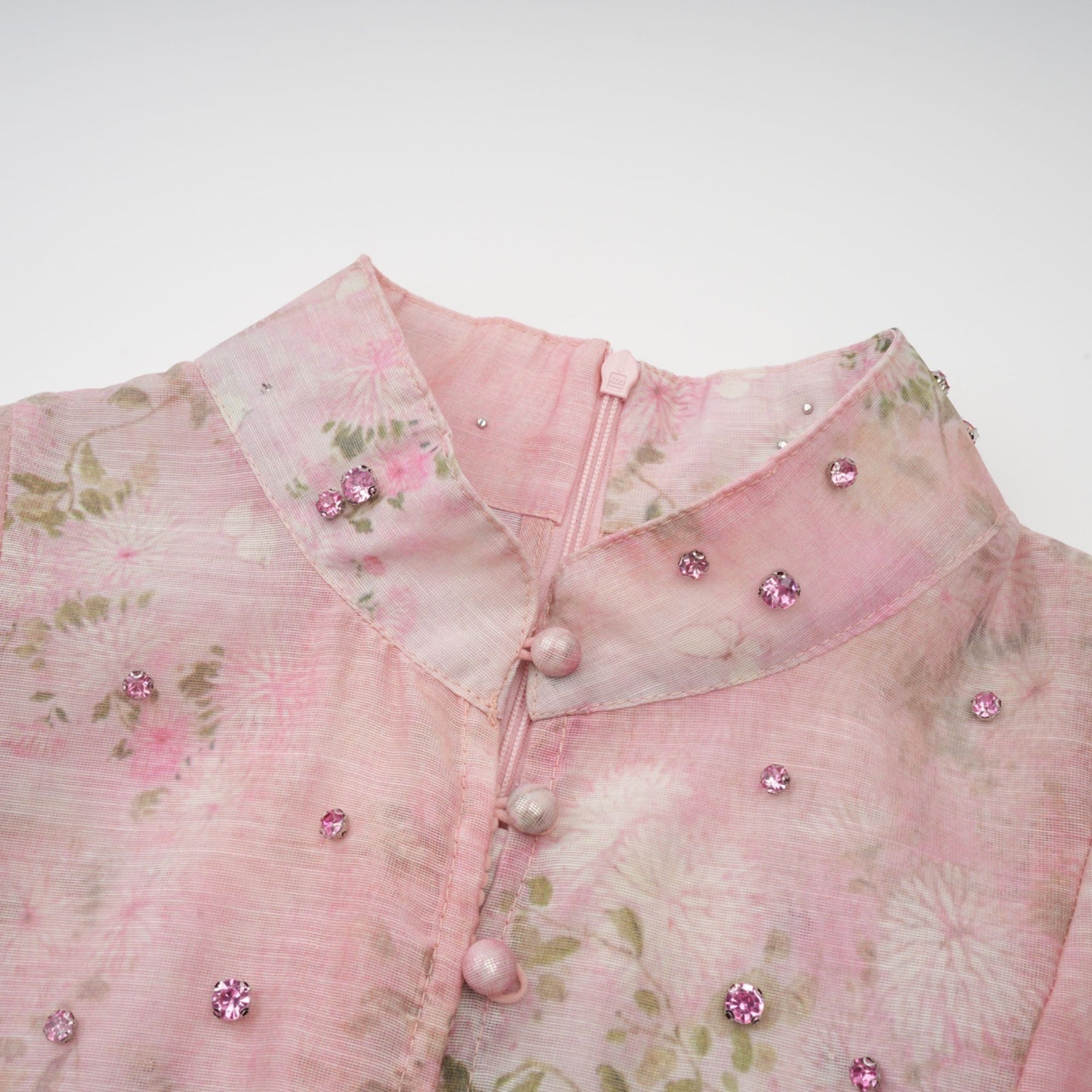 Woman wearing a pink midi dress with floral print and embellishments standing in a neutral background
