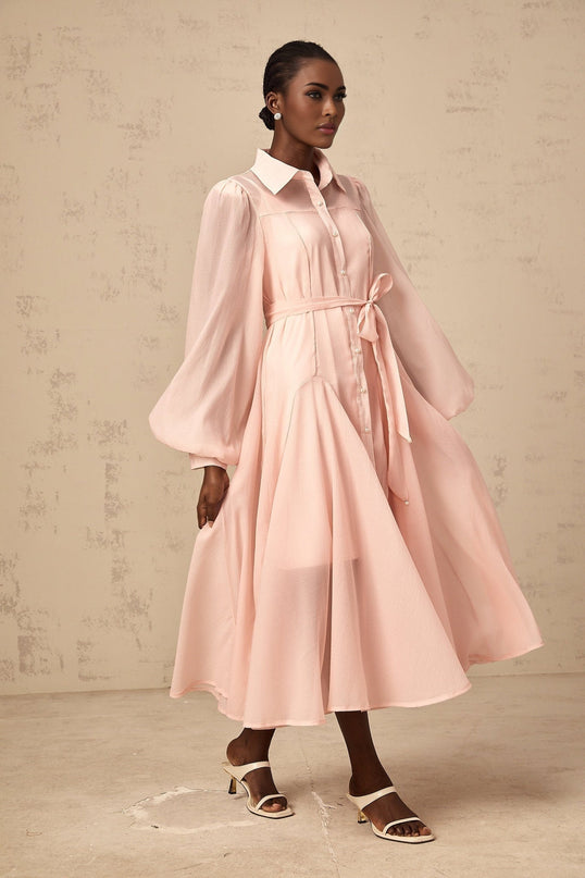 Woman wearing a pink midi length shirt dress with a tied waist detail and button front closure