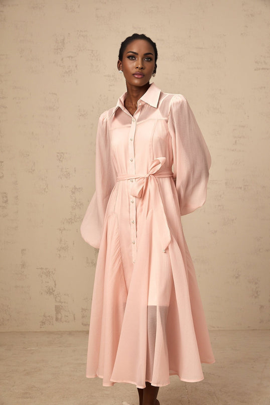 Woman wearing a pink midi length shirt dress with tied waist detail and long sleeves