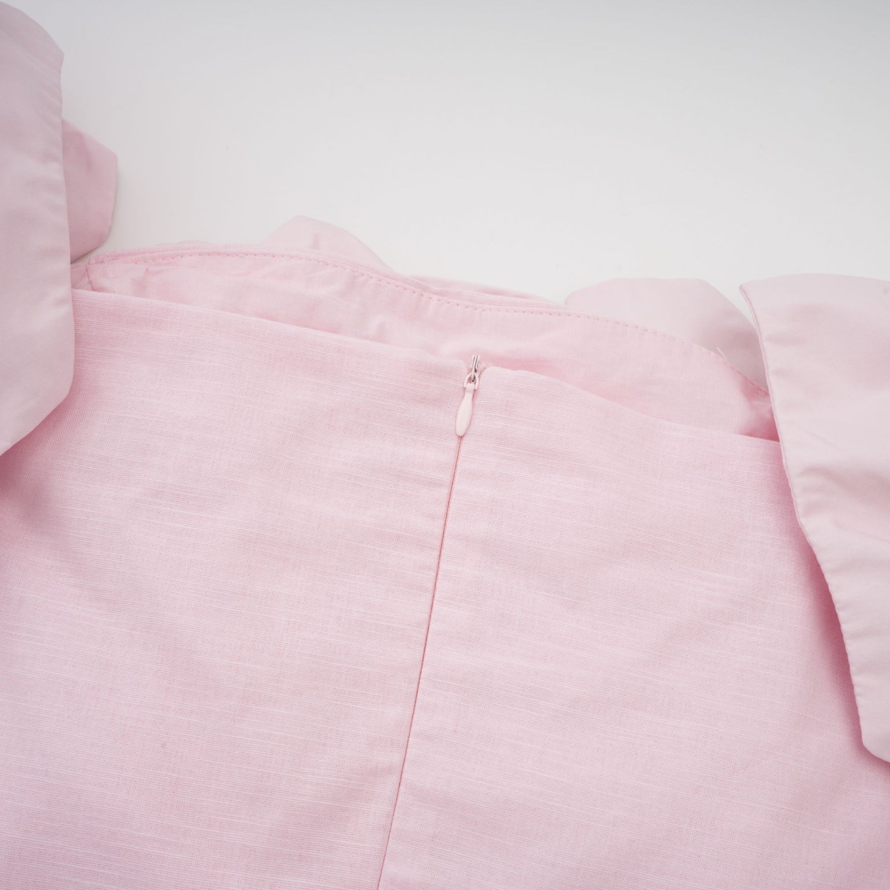 Woman wearing a pink offshoulder mini dress with 3D petal details The dress has a fitted silhouette and falls above the knee The model is shown standing against a plain background