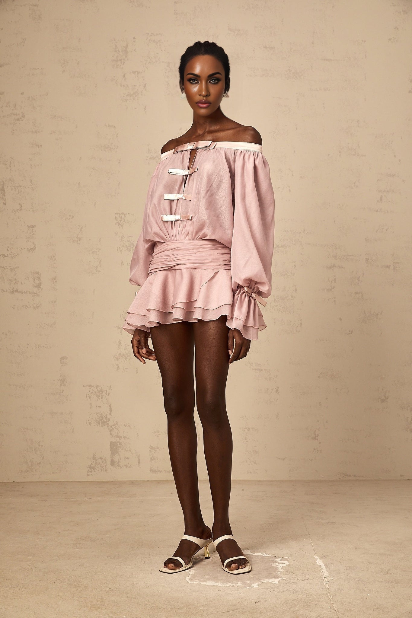 Woman wearing a pink offshoulder mini dress with a bow detail and ruffled hem