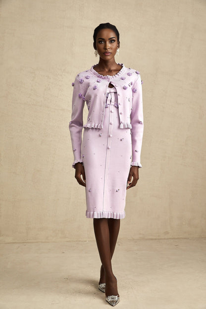 Woman wearing a purple knitted cardigan over a matching dress with faux flower embellishments on both pieces