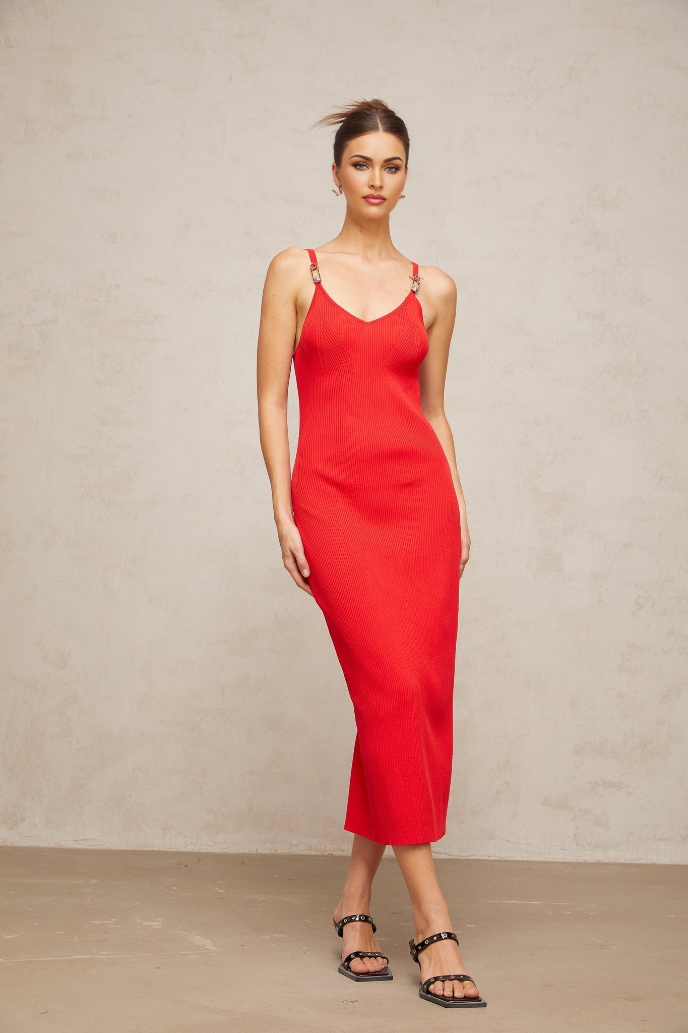 Woman wearing a red knitted midi dress with pin details standing in a neutral pose