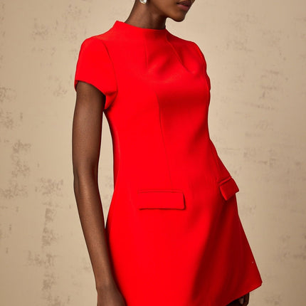 Woman wearing a red mini dress with cap sleeves standing against a plain background